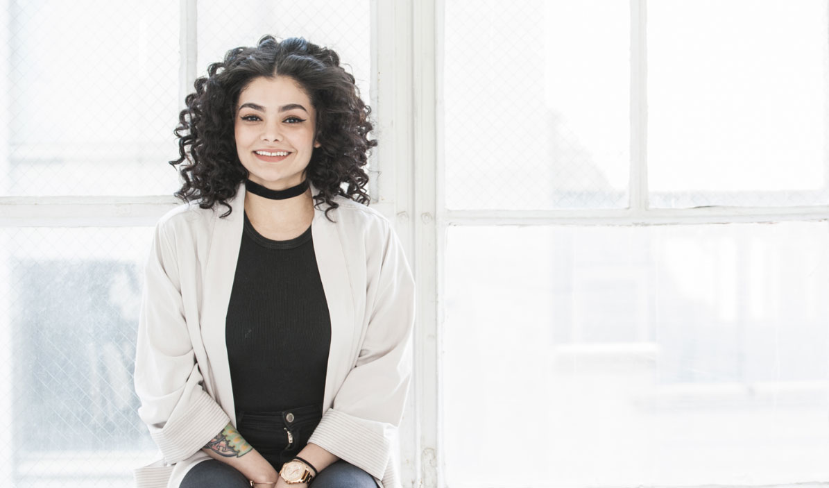 Sharp-dressed woman with styled curly hair sits in brightly lit city window. She's visiting the best dentist downtown NYC.