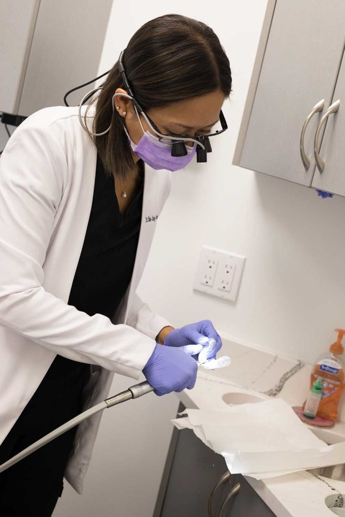 Dental assistant, wearing magnifiers over her glasses, works on an Invisalign tray.